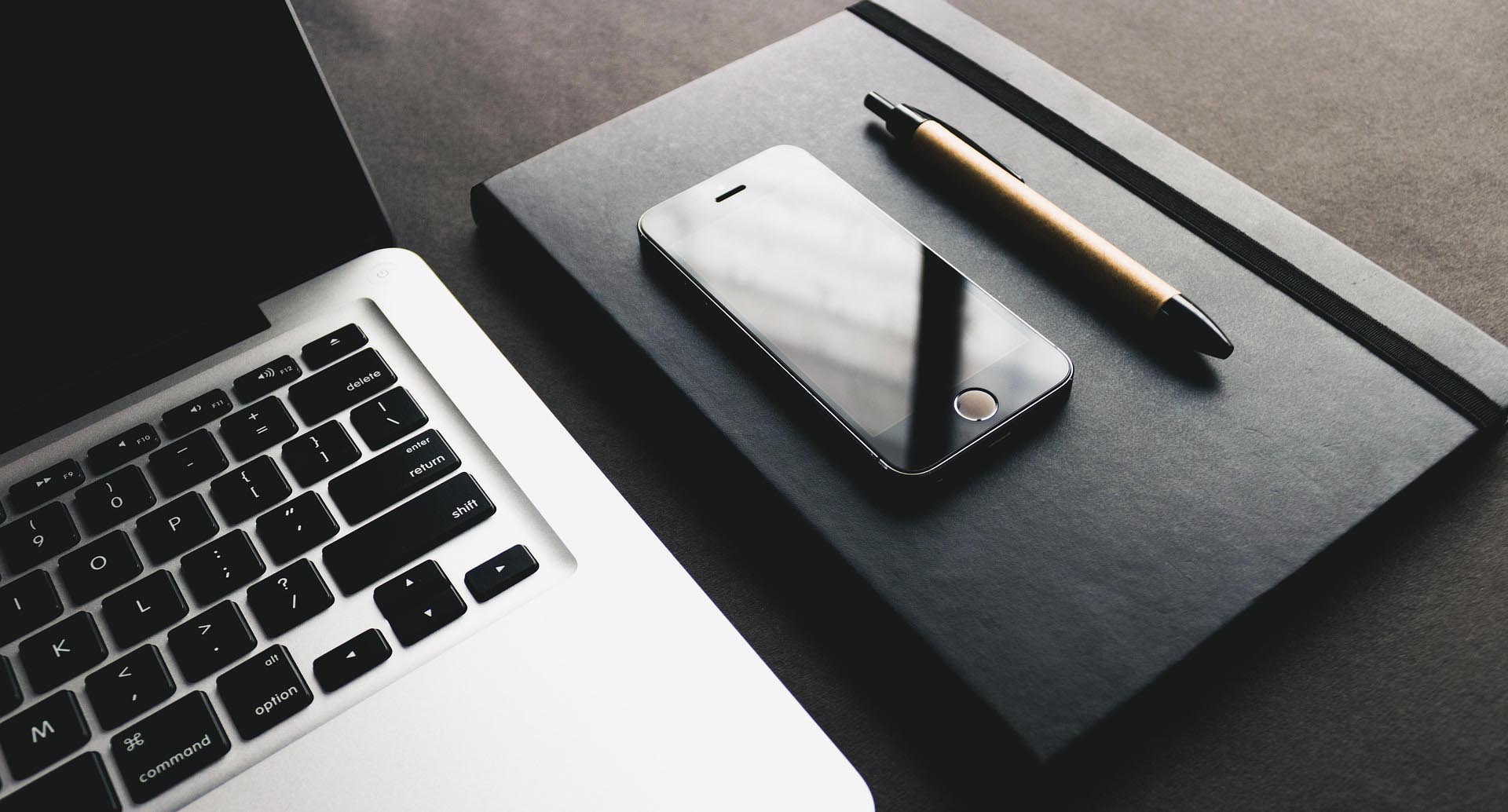 Profesjonalny workspace do projektowania logo dla firm – laptop, notatnik z piórem i telefon podkreślający kreatywność i indywidualne podejście do projektów.